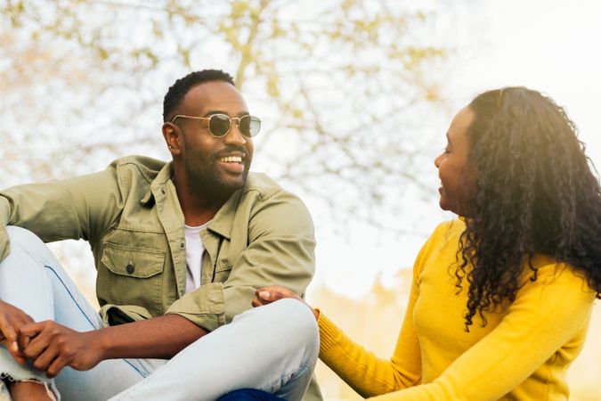 Black couple talking sitting on the grass in a park
