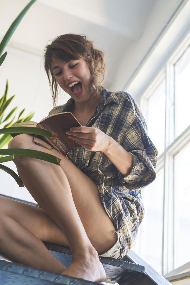 Excited female reading book on stairs in bright room