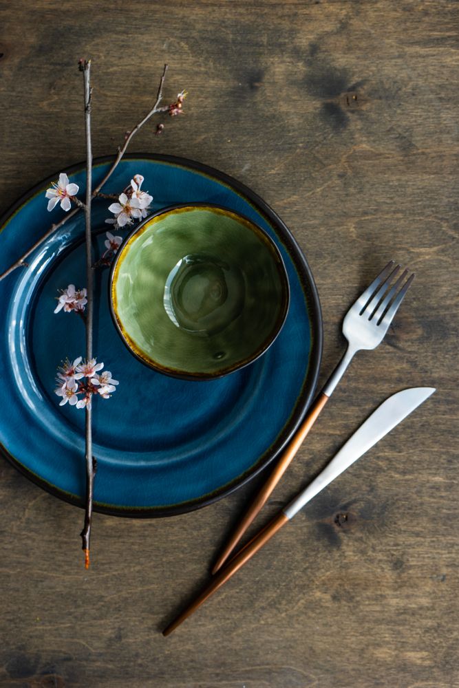 Top view of table setting with small bowl on ceramic navy plate and delicate cherry blossom branch