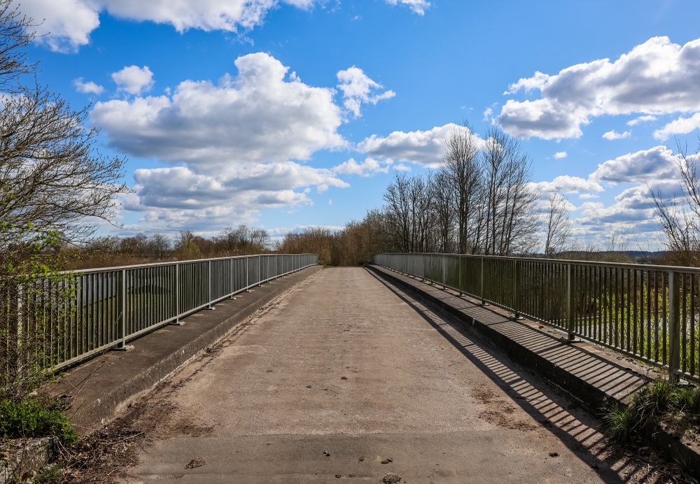 Narrow bridge with metal railing crossing a river in spring