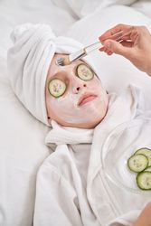 Unrecognizable woman applying mask on face of child with brush