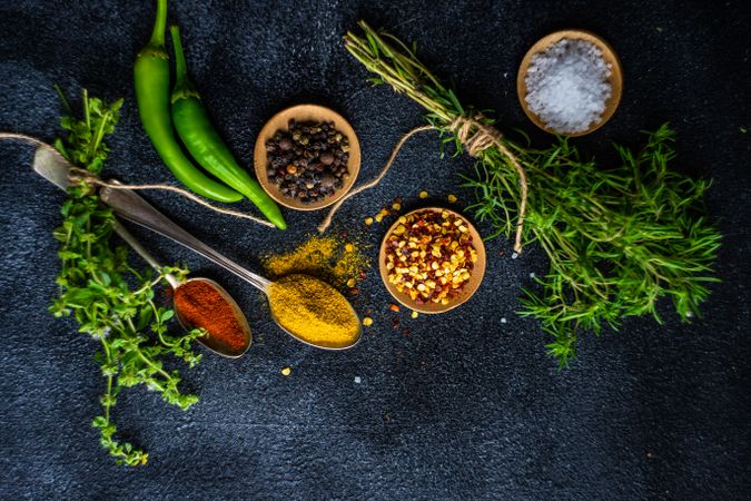 Cooking concept with pepper, herbs, oil and seasoning on dark counter