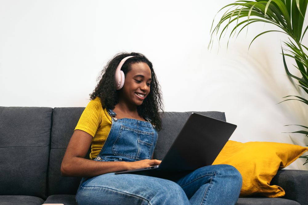 Young Black woman working with laptop and enjoying music at home