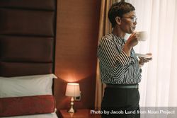 Woman in business wear standing in hotel room and having a cup of coffee 5oEA8b