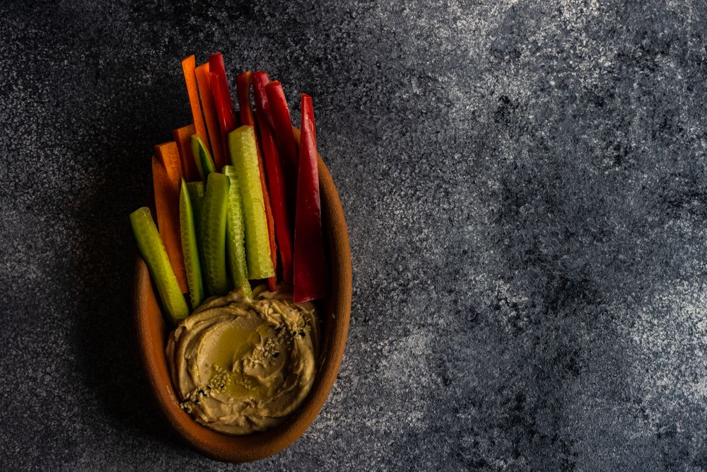 Top view of hummus dish served with chopped veggies on grey counter with copy space