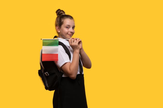 Schoolgirl carries Italian flag on backpack while posing confidently.