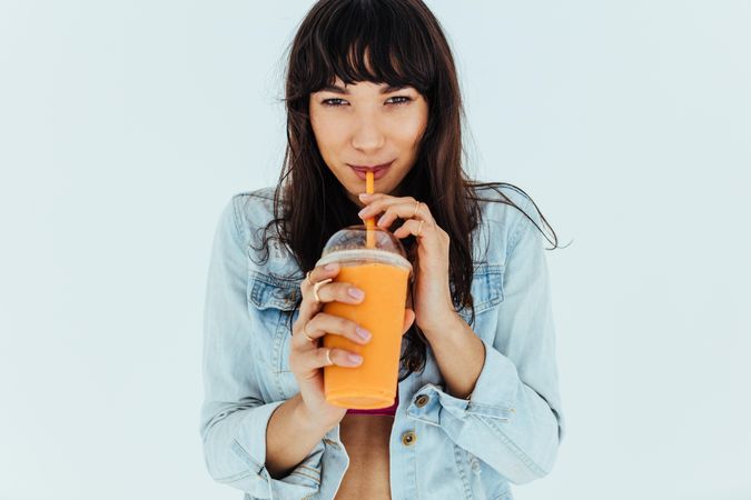 Portrait of attractive woman over light background drinking fresh fruit juice