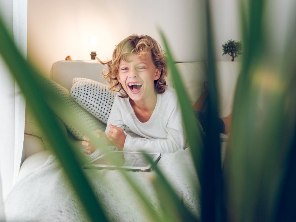 Excited boy lying on sofa watching video on tablet