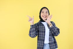 Happy Indonesian Young Woman in Veil or Hijab, Pointing at Copy Space with Right Hand