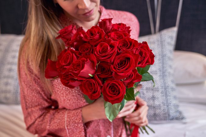 Crop positive woman with bouquet of red roses in bedroom