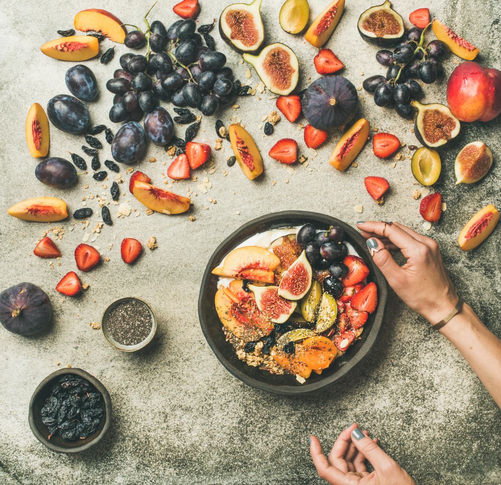 Woman with bowl of yogurt over table of figs, peaches, and chia seeds, square crop