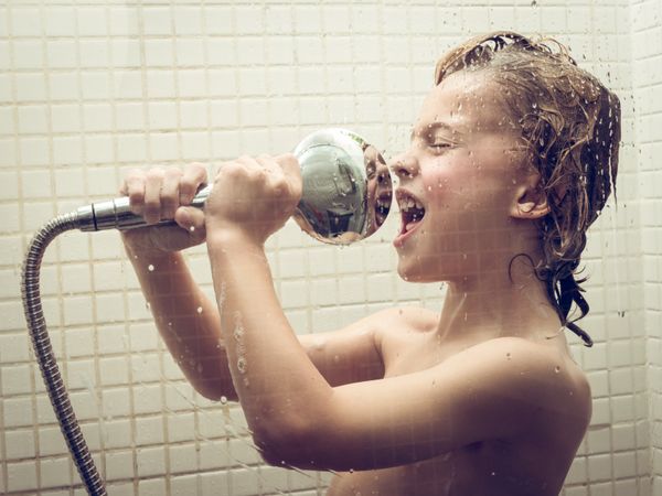 Boy singing with shower head in bathroom