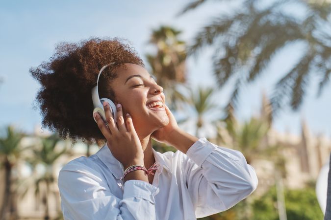 Happy Black female listening to music on street near tall palm trees