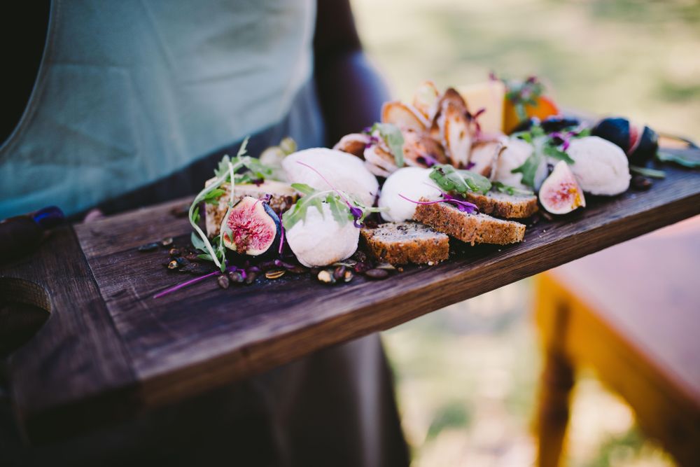 Charcuterie board with cheese, figs, bread and nuts held by a server