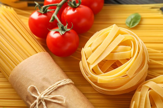 Composition with pasta, tomatoes and basil on wooden background, closeup