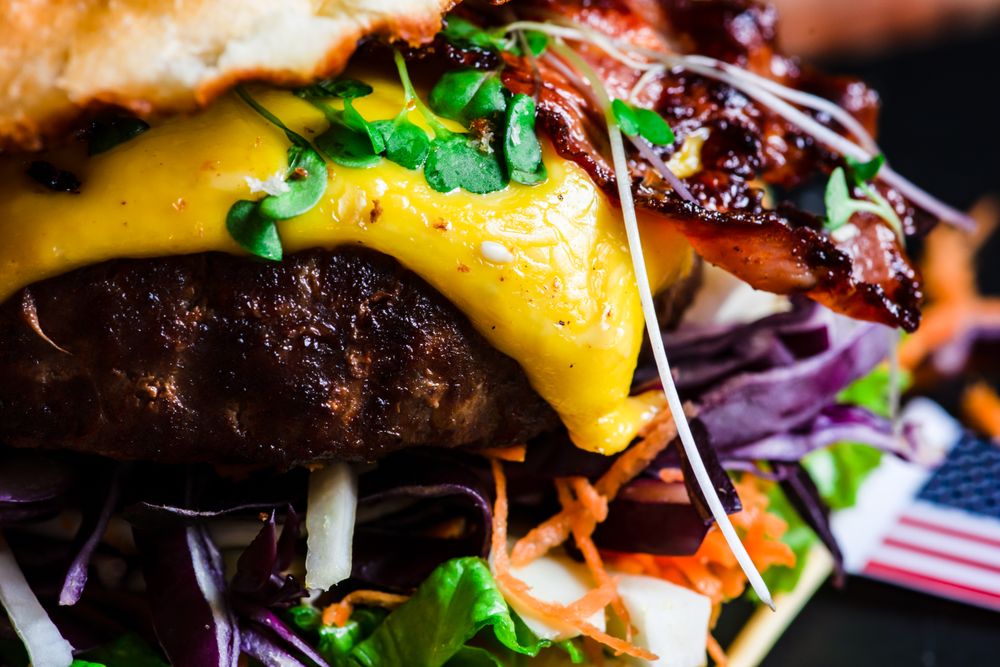 Close up of sprouts on bacon burger with melted cheese and vegetables