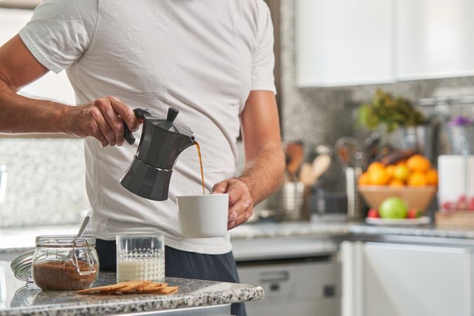 Crop man pouring coffee from moka pot in cup