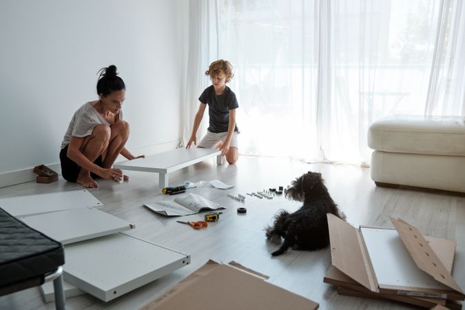 Woman and child assembling furniture in apartment with dog
