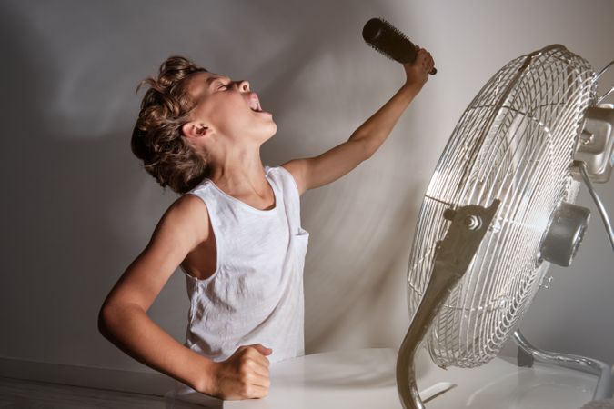 Funny boy singing into comb in front of working fan