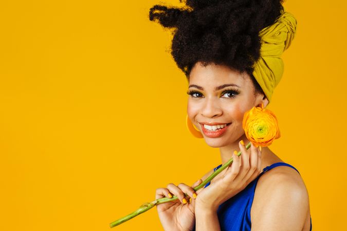 Portrait of happy Black woman with large earrings holding a rose to her face