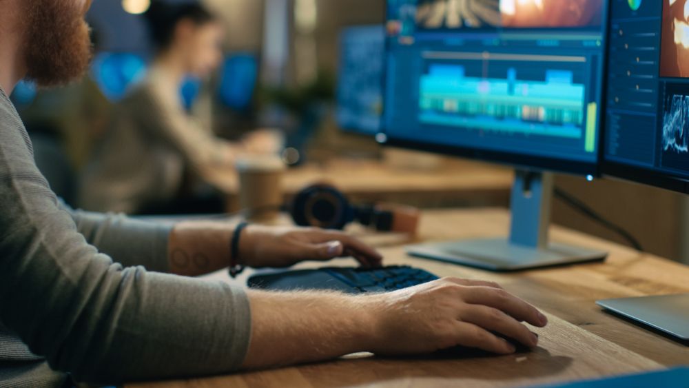Male Videographer Edits and Cuts Footage and Sound on His Personal Computer with Two Displays.