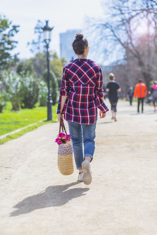 Rear view of a young hipster woman walking in a park in sunny day while holding a wicked basket