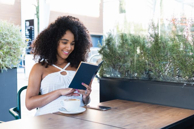 Pregnant Black woman reading book and drinking coffee
