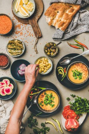 Spread of yellow lentil soup bowls, with bread, vegetable garnishes with man reaching for garnish