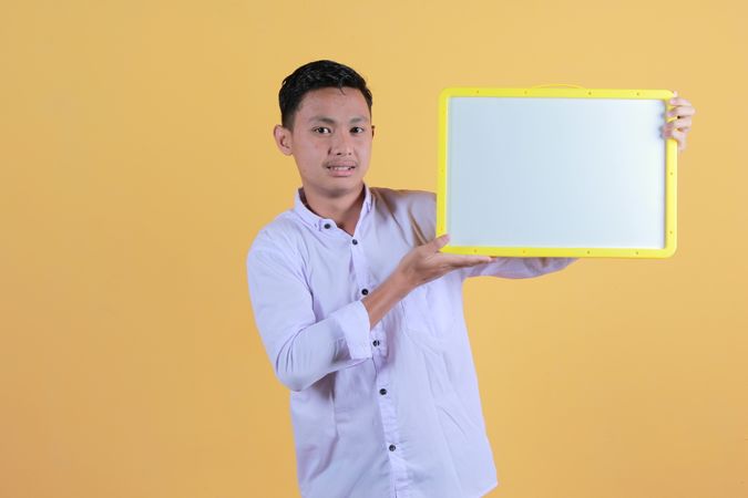 Portrait of a young man in yellow backdrop holding a blank note board