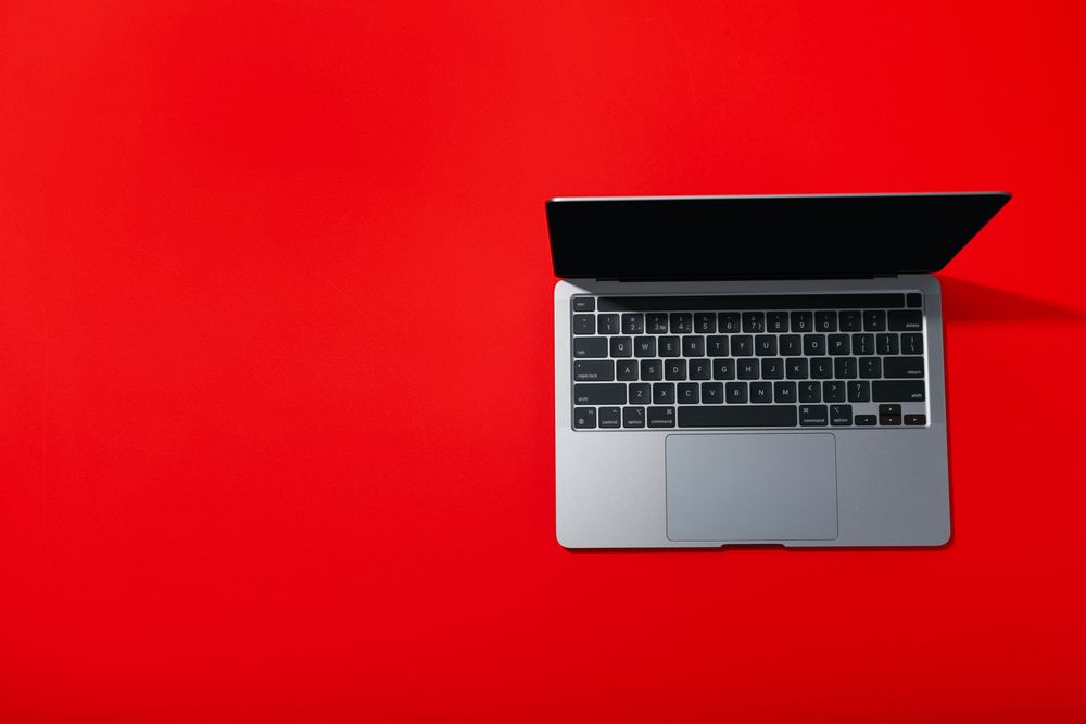 Top view of opened silver laptop and keyboard on red desk with copy space