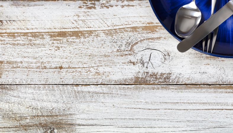 Partial dinner table setting with cutlery and dark blue plate on rustic wood table
