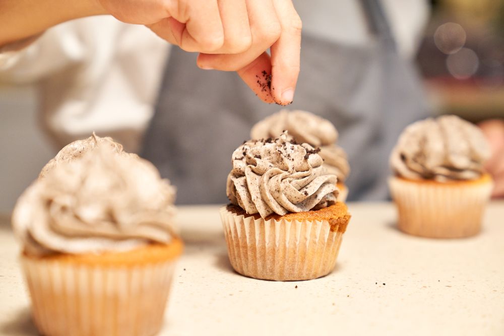 Faceless chef decorating cupcakes on table