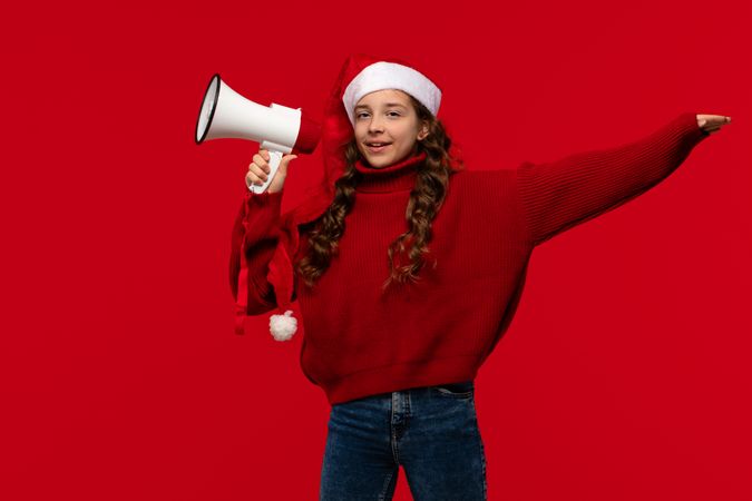 Smiling girl in Santa hat and red sweater holds megaphone