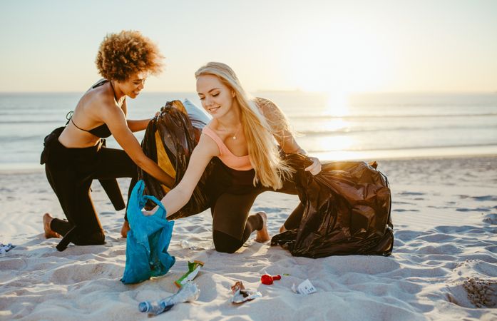 Young female surfers collecting trash in garbage bags from the beach