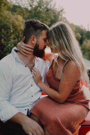 Loving couple sitting on car on road near forest