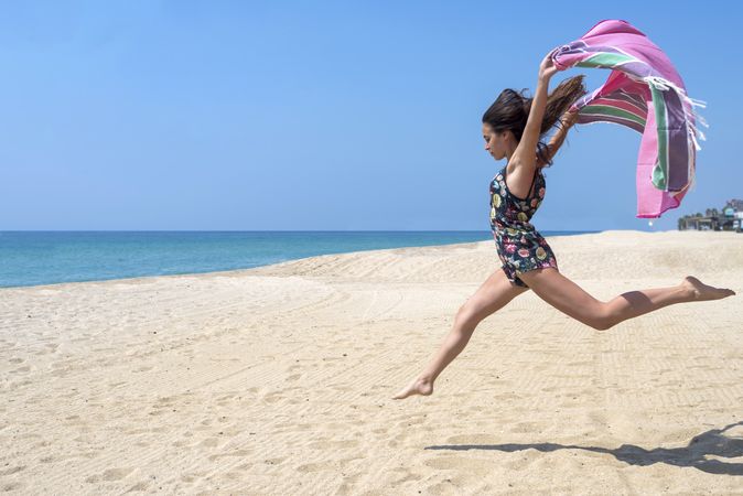 Woman jumping in sand with sarong