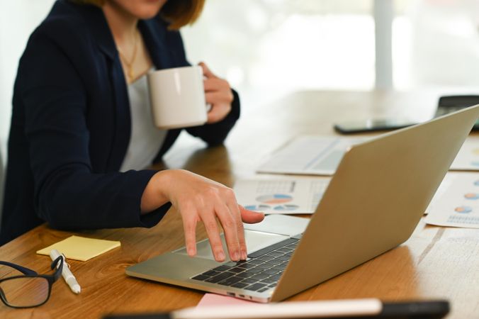 Young woman's hand using laptop keyboard and drinking coffee