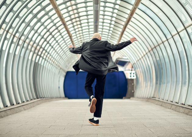 Young man dancing in long glass public corridor