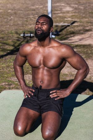 Strong Black sportsman breathing during training on sports ground