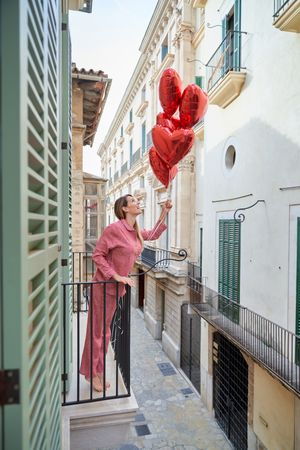 Woman on balcony pretending to launch heart balloons