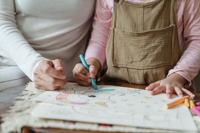 Cropped image of adult and child drawing with crayon