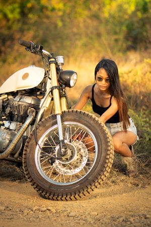 Woman fixing motorbike in countryside