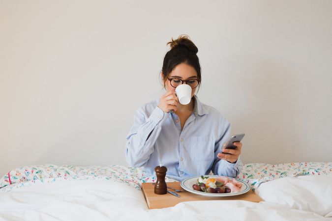 Young woman with breakfast on bed using smart phone