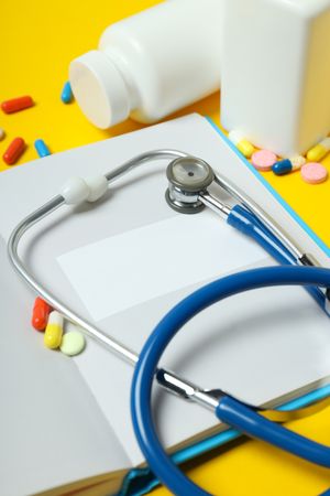 Notepad, stethoscope and jars of pills on yellow background, close up