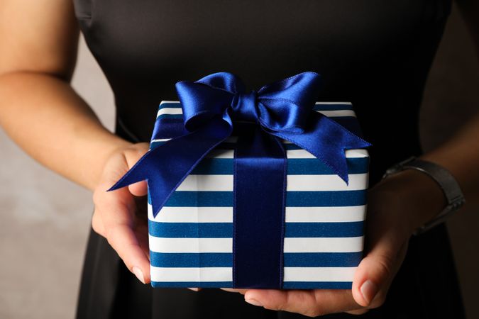 Young woman holding gift box with blue bow, close up