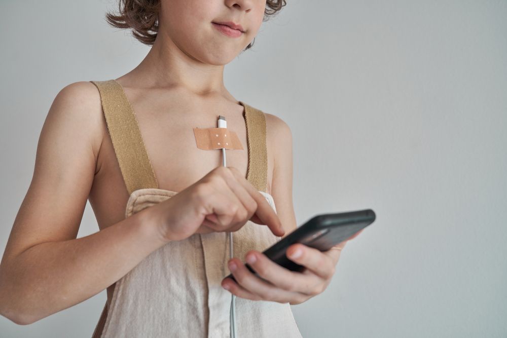 Unrecognizable kid with charger on chest using smartphone