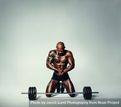 Muscular man working out kneeling in front of heavy weights 4jVGpr