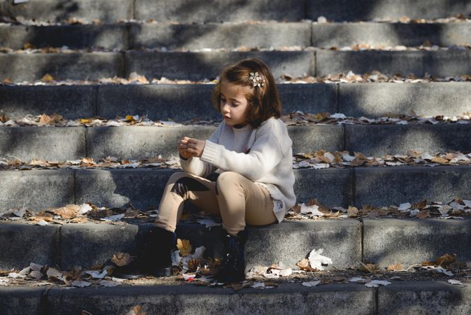 Child sitting on cement steps in outdoor park with fall leaves