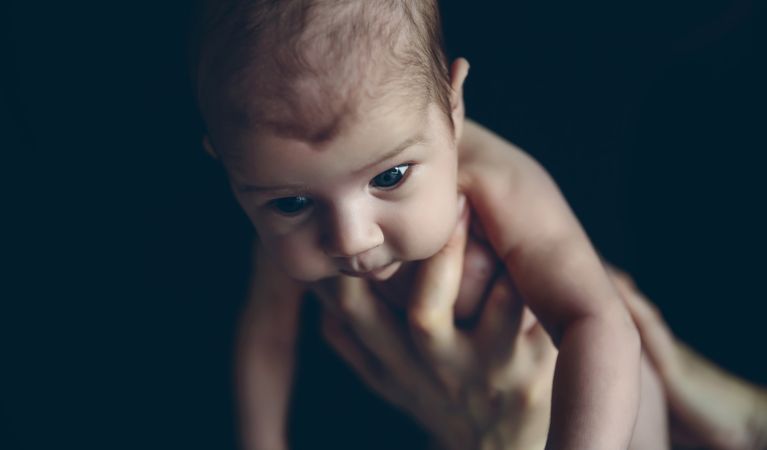 Newborn baby girl held by one hand