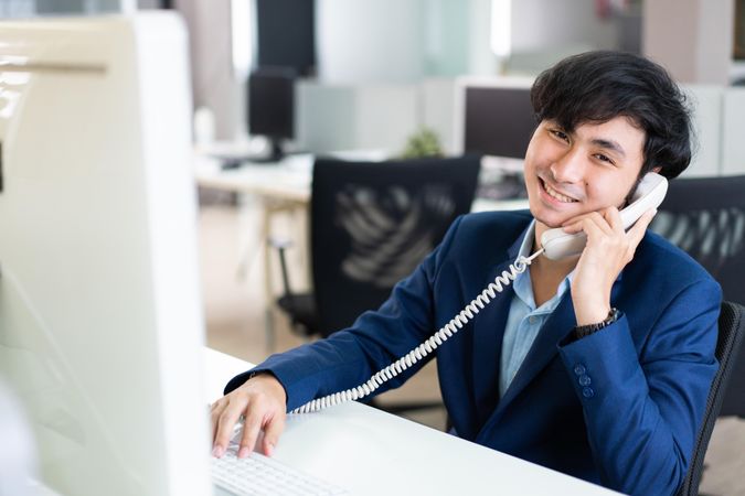 Smiling Asian male in suit on satisfying phone call at work